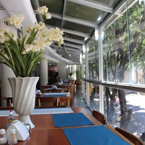 A restaurant with tables, chairs, and a large window with a view of trees. - Real Minas Suites Hotel (Governador Valadares)