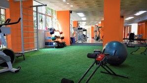A gym with exercise equipment, green artificial turf, and orange walls. - Real Minas Suites Hotel (Governador Valadares)