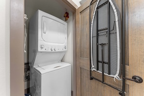 A laundry room with a front-loading washer and dryer, a wooden door with a mesh window, and a small decorative item above the door.