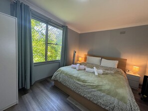 A hotel room with a large bed, two bedside tables, a window with curtains, and a view of greenery outside. - Entire villa in Metford, 
A relaxing, homey stay — ideal for short breaks (Metford)