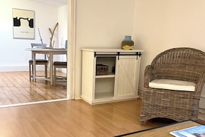 A room with a wooden floor, a wicker chair, a white cabinet with a fish-shaped object on top, and a framed picture on the wall. - Your comfortable apartment, Alter Konsumverein, Apartment 1, in a central location on Sylt (Sylt)