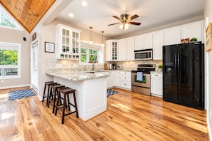 A modern kitchen with white cabinets, a black refrigerator, stainless steel appliances, wooden flooring, and a ceiling fan. - 🌊 Beechnut Cove | Lake Gaston Escape • Private Dock • Game Room • Fire Pit 🔥 (Littleton)