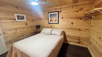 A wooden-paneled room with a bed, a nightstand, a lamp, and two framed pictures on the wall.
