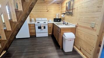 A kitchen with wooden walls, a dark wooden floor, a white stove, a sink, and a trash bin.