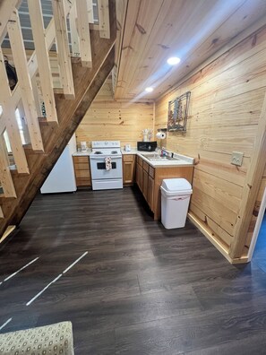 Une cuisine avec des murs en bois, un plancher en bois foncé, une cuisinière blanche, un évier et une poubelle.