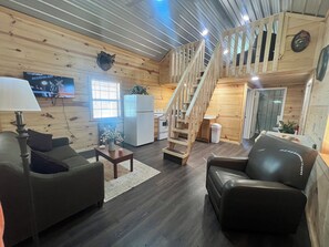 Interior acogedor de una cabaña con detalles de madera, un comedor, una cocina y una escalera que sube a un nivel superior.