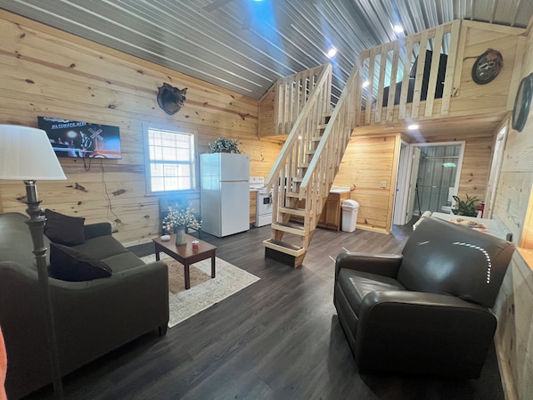 Interior acogedor de una cabaña con detalles de madera, un comedor, una cocina y una escalera que sube a un nivel superior.