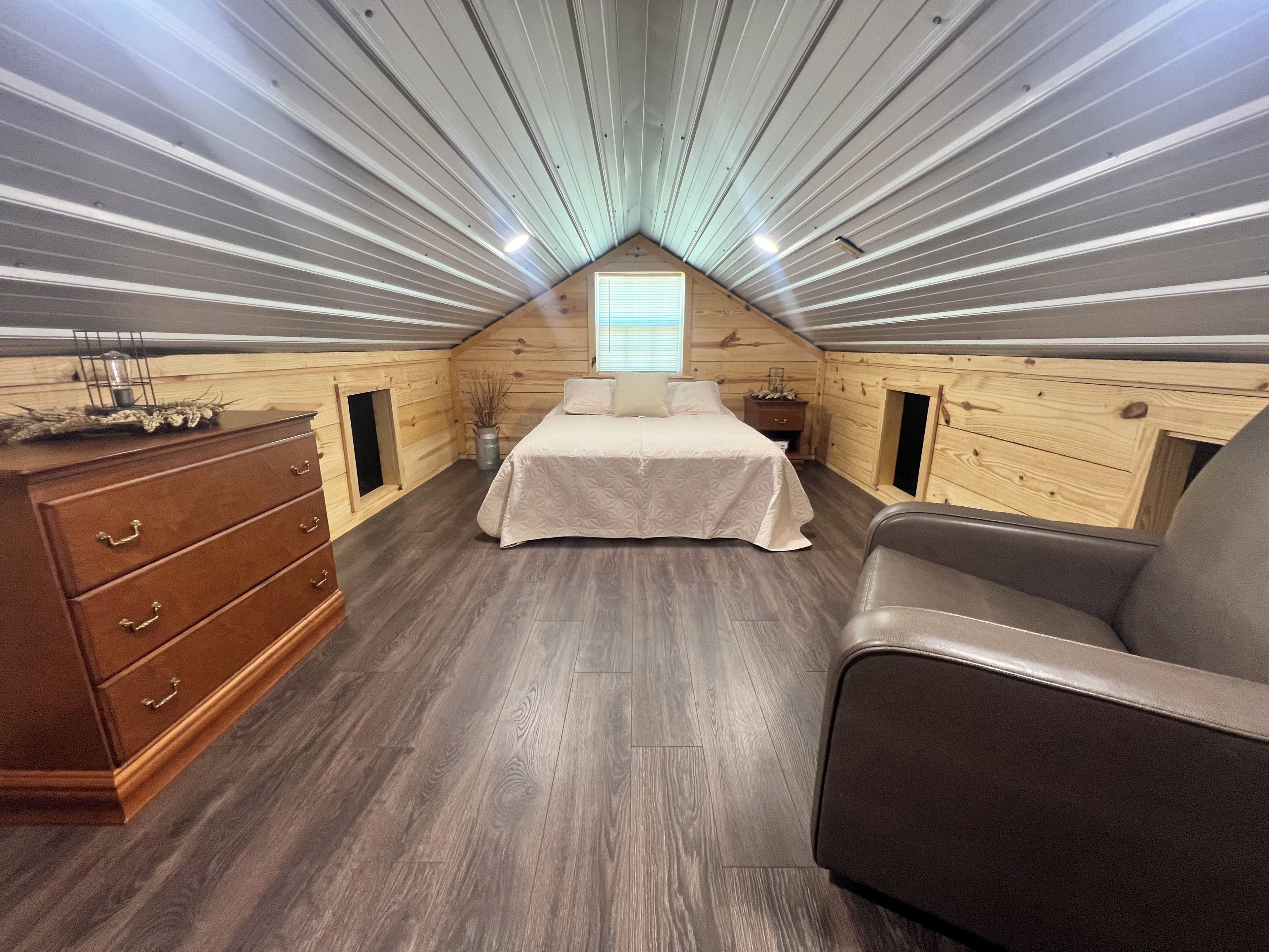 A bedroom with a sloped ceiling, a bed, a dresser, and a chair.