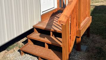 A wooden deck leading to a white door of a corrugated metal building.