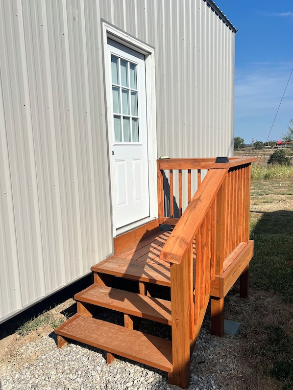 A wooden deck leading to a white door of a corrugated metal building.