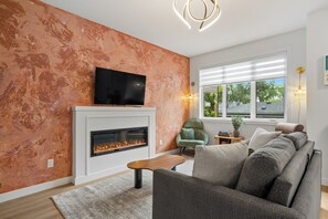 A modern living room with a fireplace, a flat-screen TV, and a sofa. - Leave the car parked. Edmonton's best cafés & restaurants are minutes' walk away, downtown 5 by car. Your brand-new upper home: gallery walls, chef-style kitchen with a gas range, fireplace, A/C & patio. For professionals & families, room for 9. (Edmonton)