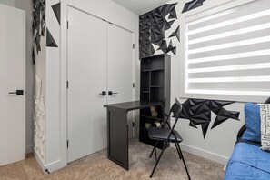 Et værelse med en hvid dør, et sort skrivebord, en blå sofa og en væg med et geometrisk mønster.