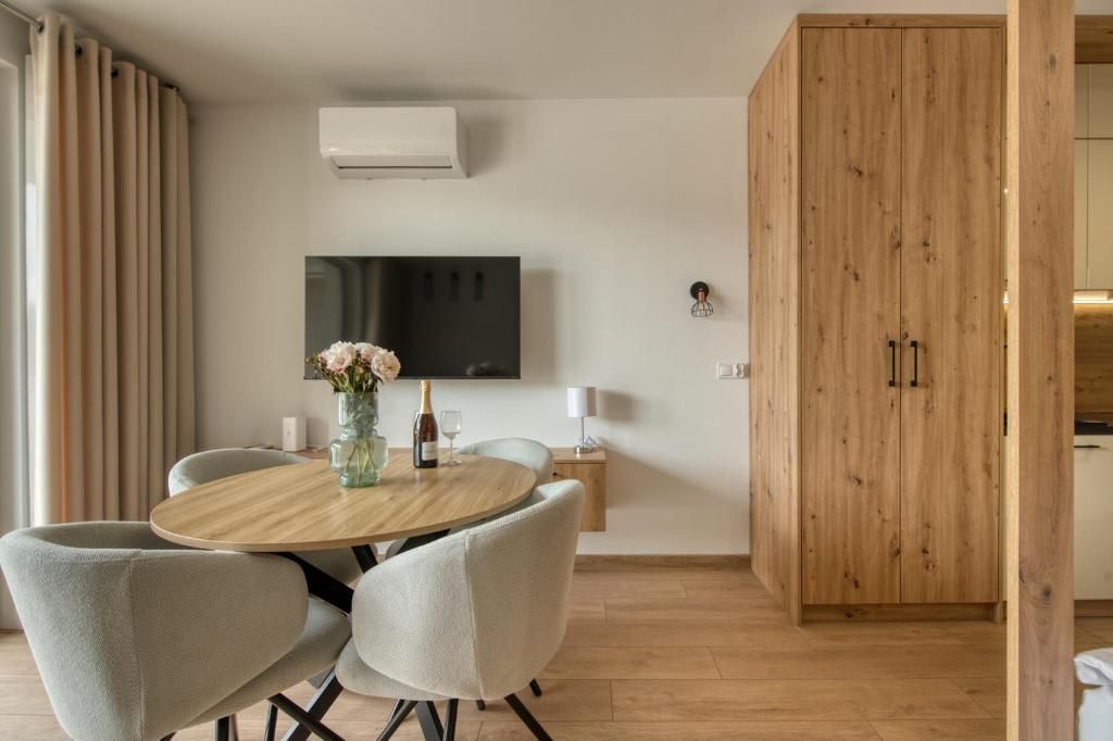 Ein modernes Wohnzimmer mit einem runden Holztisch, grau gepolsterten Sesseln, einem flachbildfernseher an der Wand und einem Holzschrank.