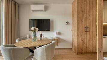 Ein modernes Wohnzimmer mit einem runden Holztisch, grau gepolsterten Sesseln, einem flachbildfernseher an der Wand und einem Holzschrank.