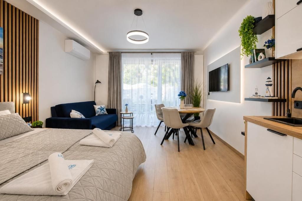 Una habitación de hotel moderna con una cama, zona de comedor, televisor y kitchenette.