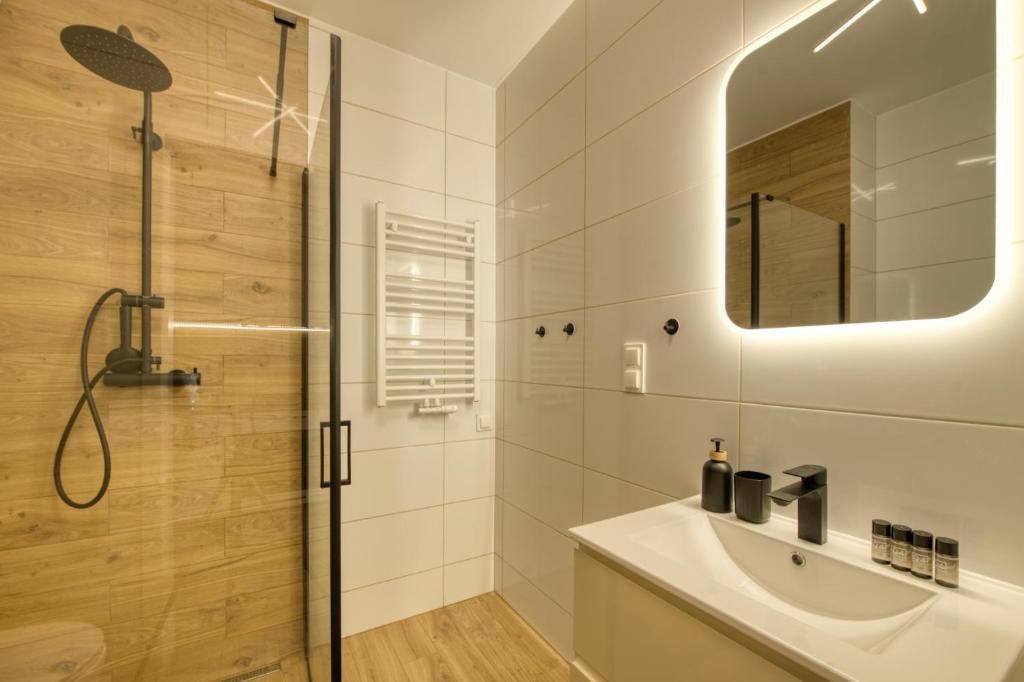 Un baño moderno con cabina de ducha de vidrio, lavamanos blanco e iluminación integrada en un espejo.