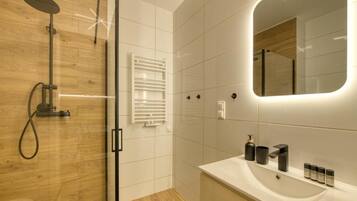 Un baño moderno con cabina de ducha de vidrio, lavamanos blanco e iluminación integrada en un espejo.