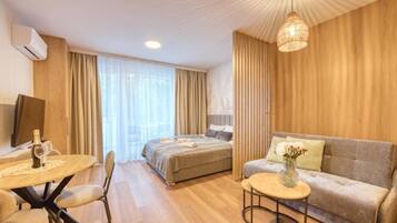 Et hotelværelse med seng, sofa, spisebord med stole, lille sofabord og en hængende lampe.