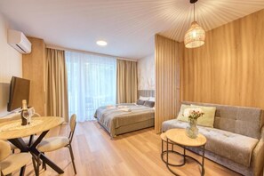 Habitación de hotel con cama, sofá, mesa de comedor con sillas, una mesita de centro y una lámpara colgante.