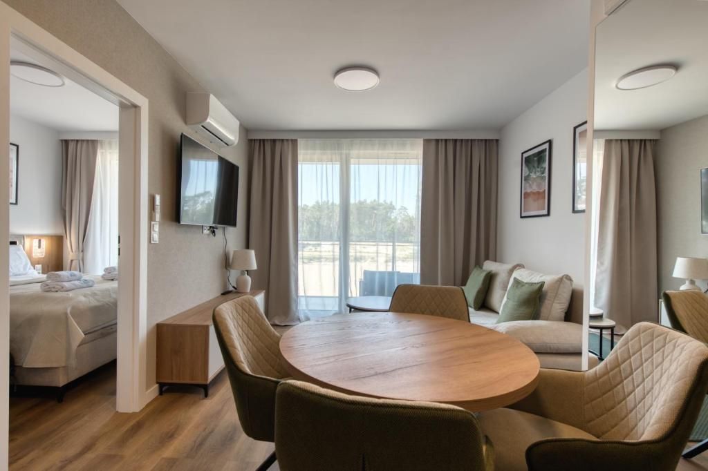 A hotel room with a bed, a round dining table, chairs, a TV, and a balcony with curtains.