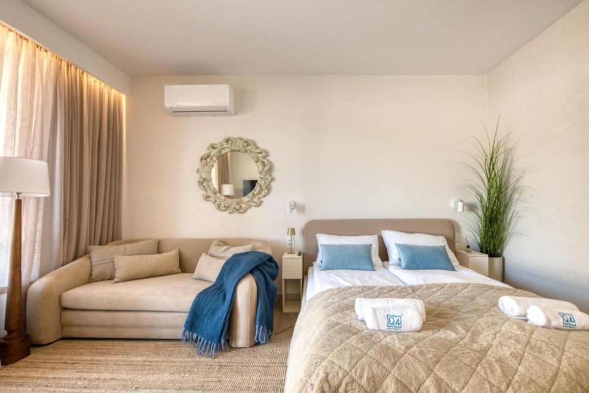 Een hotelkamer met een bed, een bank, een spiegel, een airconditioner en een plant.