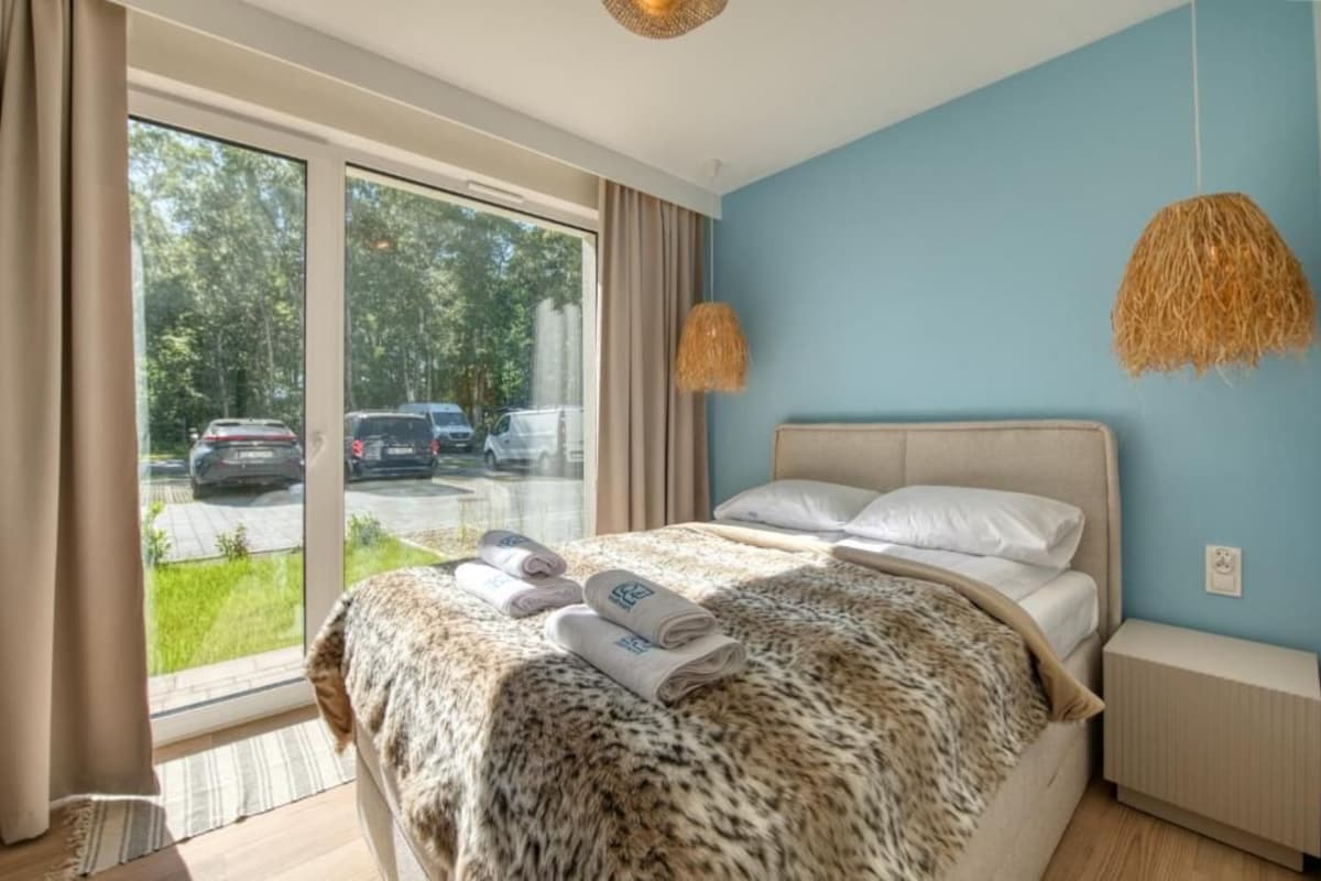 Een slaapkamer met een groot raam, een bed met een luipaardprint hoes en twee hanglampen.