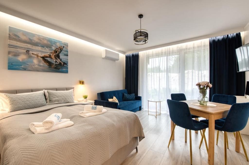 A modern hotel room with a large bed, a dining table with chairs, a TV, and a painting on the wall.