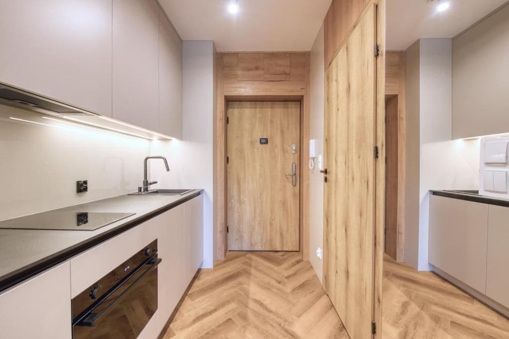 A modern kitchen with a wooden door, white cabinets, and a herringbone floor pattern.