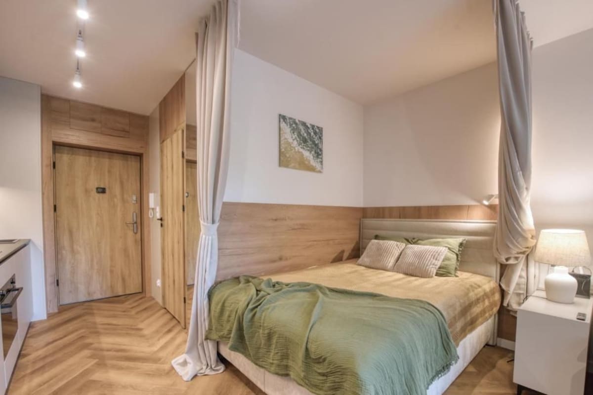 Een slaapkamer met een bed, nachtkastje, lamp, schilderij aan de muur en een deur.