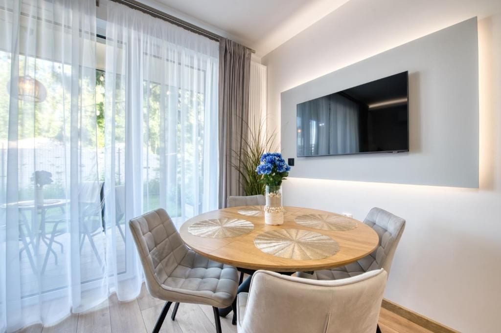 A modern dining area with a round wooden table, cushioned chairs, and a vase with blue flowers.
