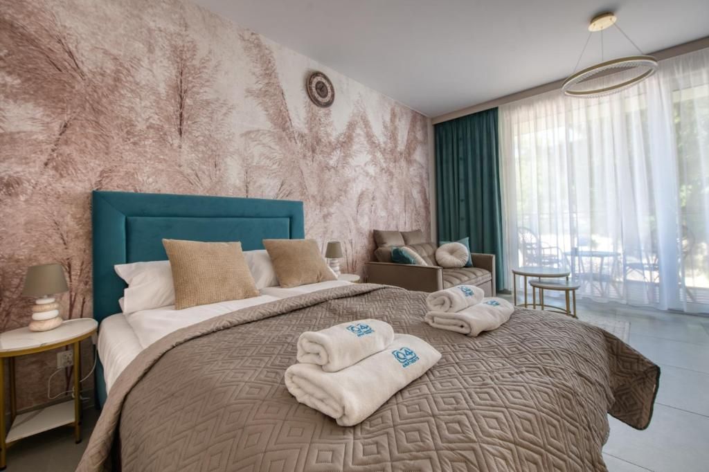 Ein Hotelzimmer mit einem großen Bett, einem Nachttisch, einer Sitzecke mit Tisch und Stühlen und Blick ins Freie durch das Fenster.