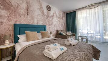 Ein Hotelzimmer mit einem großen Bett, einem Nachttisch, einer Sitzecke mit Tisch und Stühlen und Blick ins Freie durch das Fenster.