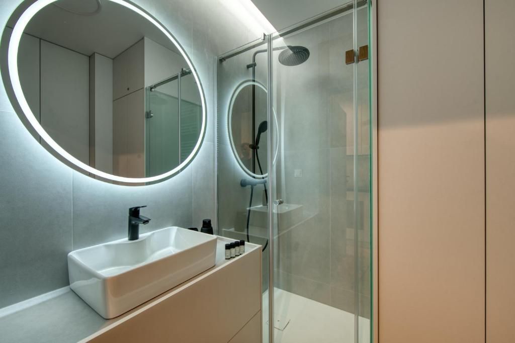 Un baño moderno con un espejo redondo, un lavamanos blanco y una ducha con cerramiento de vidrio.