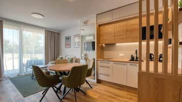 A modern kitchen with wooden cabinets, a dining area with a round table and chairs, and a large window with curtains.