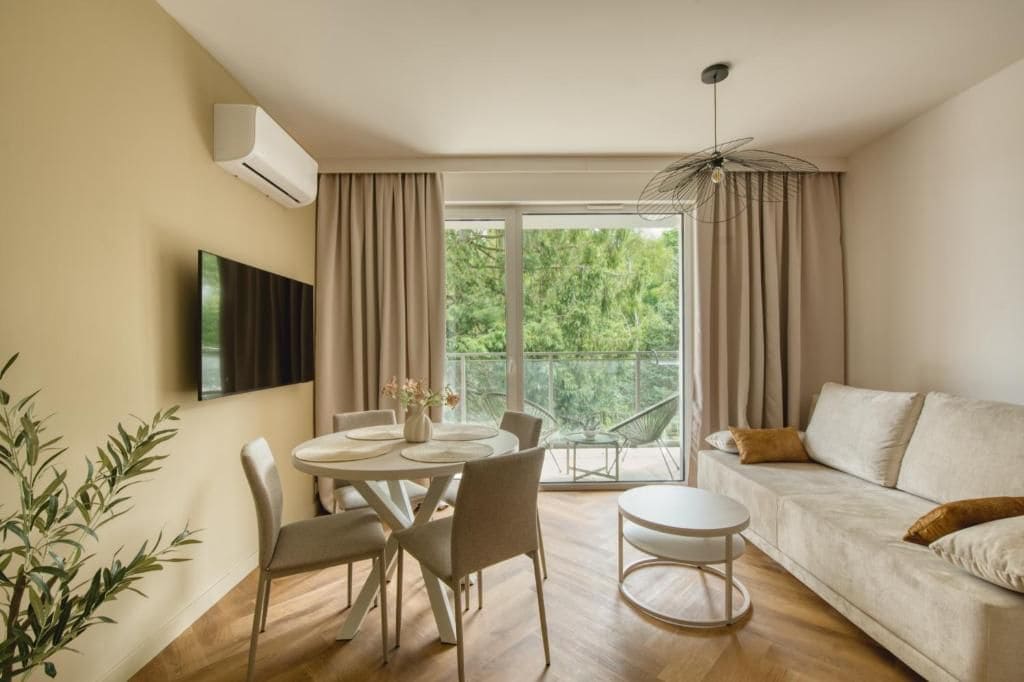 A modern living room with a dining area, a sofa, a TV mounted on the wall, and a balcony with curtains.