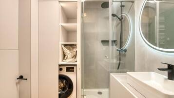 A modern bathroom with a glass-enclosed shower, a built-in washing machine, and a white sink with a mirror.