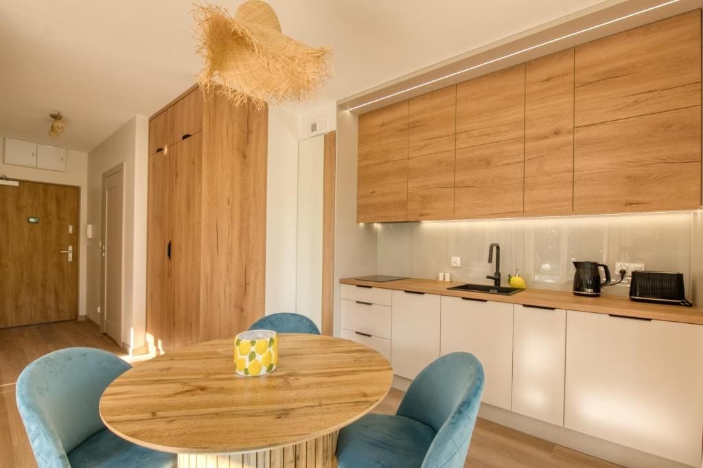 Une cuisine moderne avec des meubles de rangement en bois, une table de salle à manger ronde avec des chaises et un luminaire suspendu.