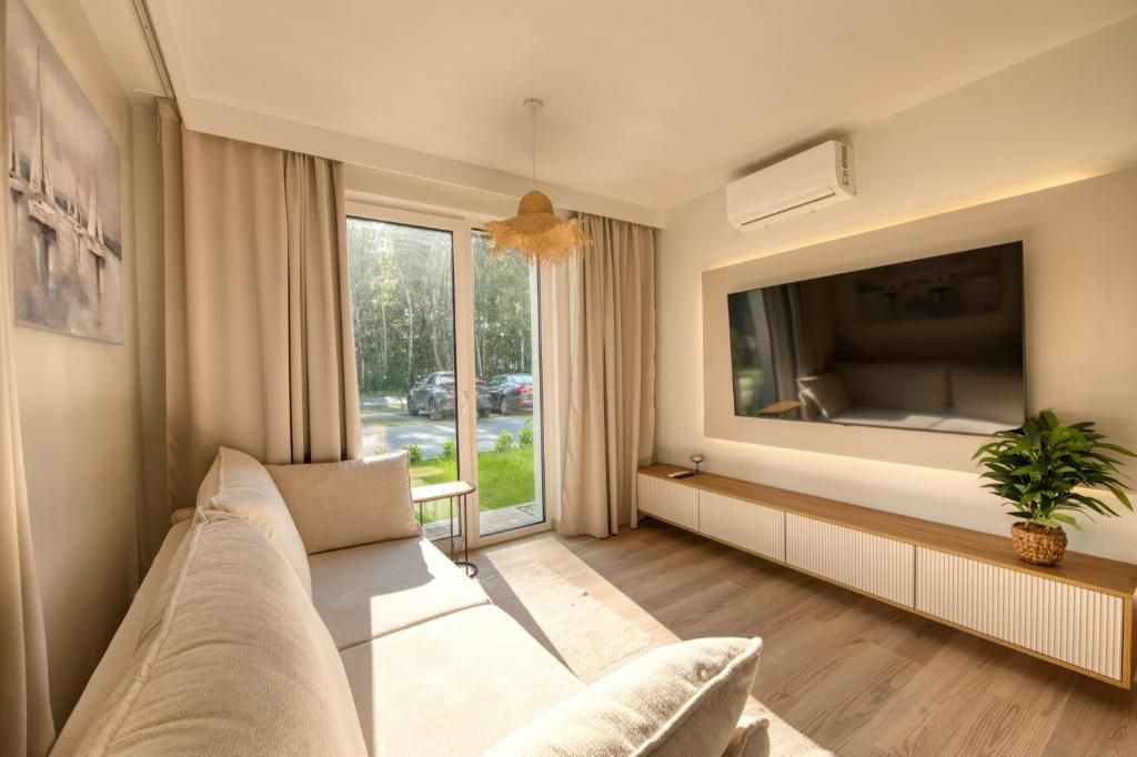 A modern living room with a sofa, a television mounted on the wall, a window with curtains, and a radiator below the TV.