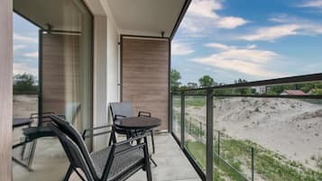 A balcony with a table and chairs, a glass door, and a view of a sandy area with a fence.