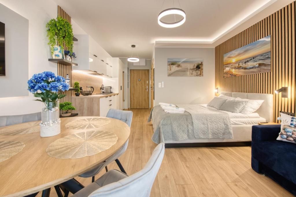 A modern hotel room with a bed, a dining table with chairs, a sofa, and a kitchen area.