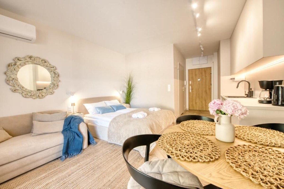 Un dormitorio moderno con cama, mesita de noche y espejo. Hay una zona de comedor con mesa y sillas.