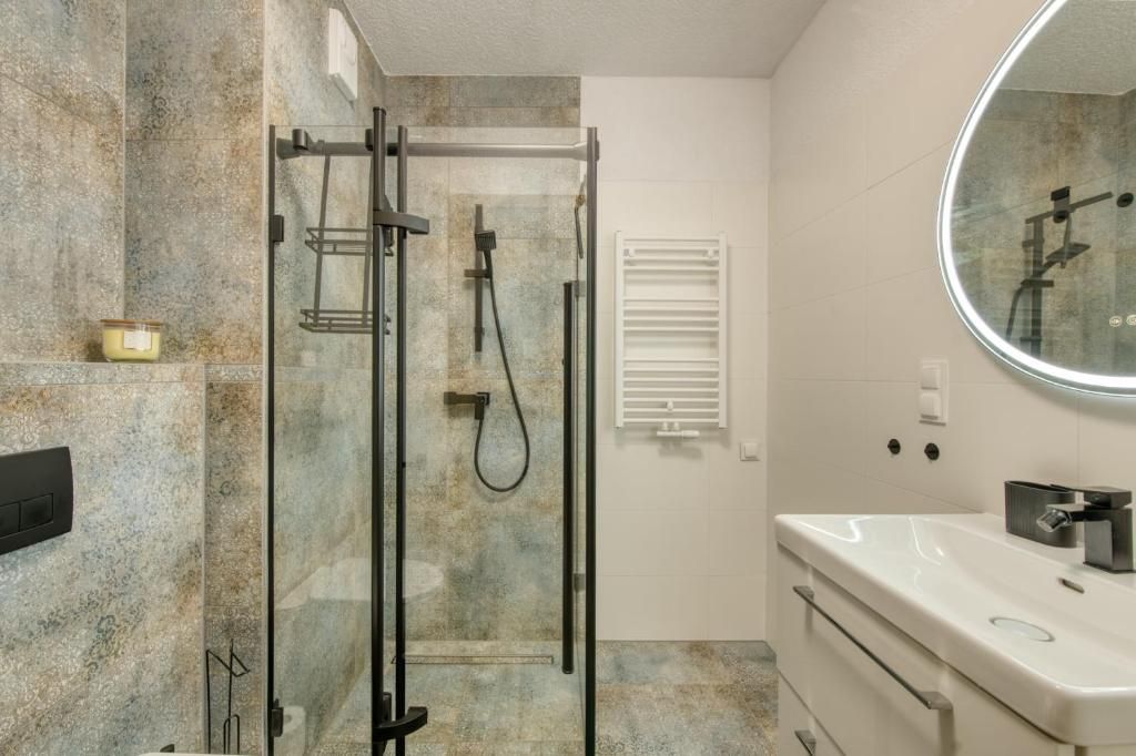 A bathroom with a glass-enclosed shower, a white sink, and a mirror.