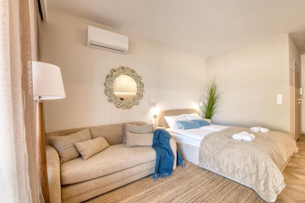 A hotel room with a bed, a sofa, a mirror, and a wall-mounted air conditioner.