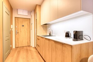 Una cocina compacta con puerta de madera, un lavamanos, una cafetera y una encimera.
