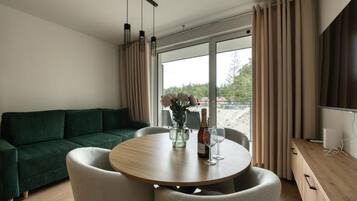 En moderne stue med en grøn sofa, et rundt træbord og et stort vindue med gardiner.