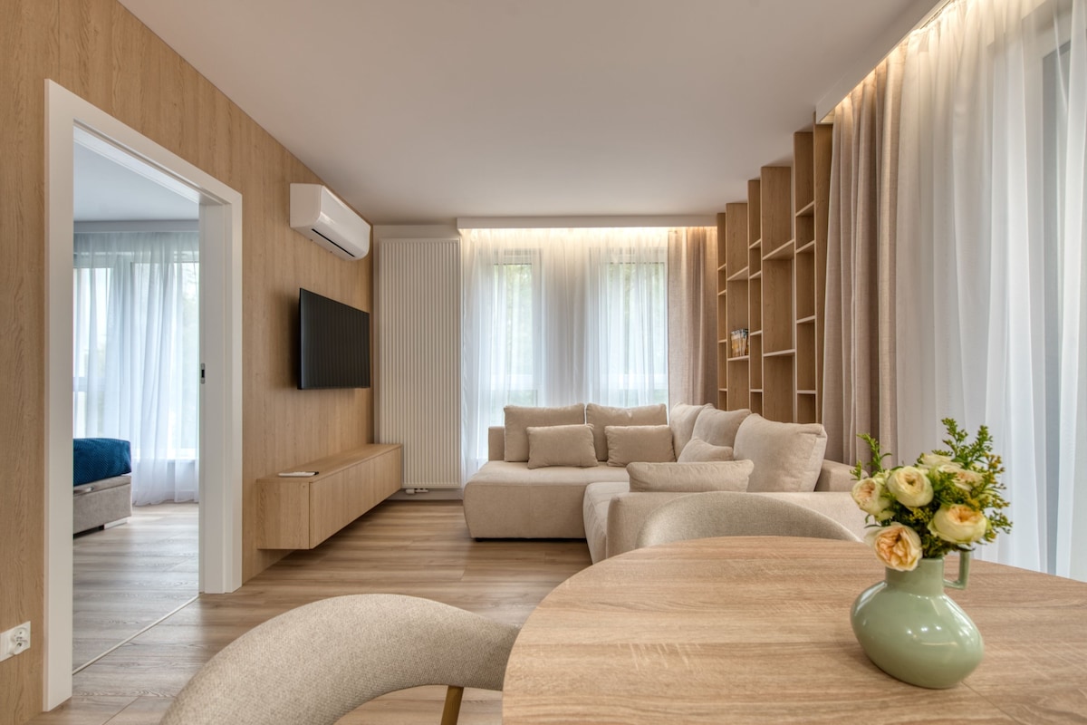 A modern living room with a sofa set, a flat-screen TV mounted on the wall, and a wooden floor.