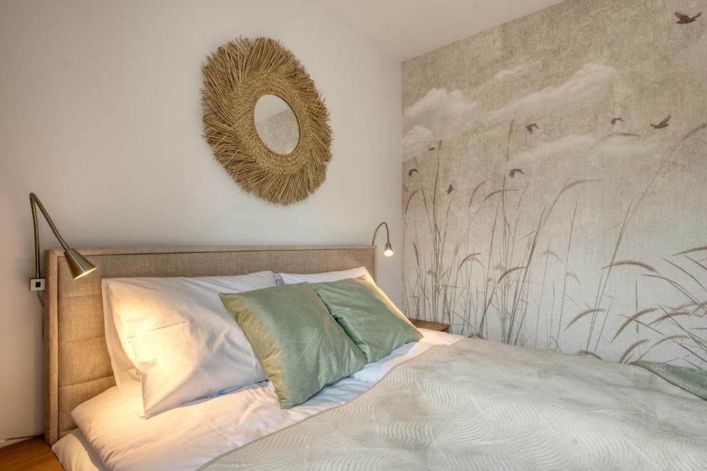 A bedroom with a bed, a wall-mounted mirror, and a wall art depicting birds and plants.