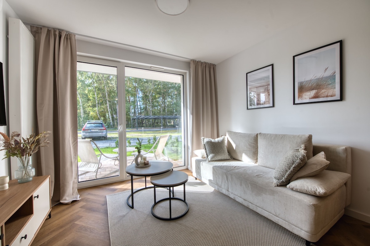 A modern living room with a sofa, a coffee table, and a view through a large sliding glass door.