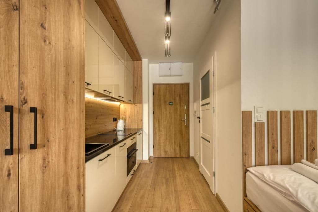 A narrow hallway with wooden flooring leading to a bedroom with a wooden headboard.