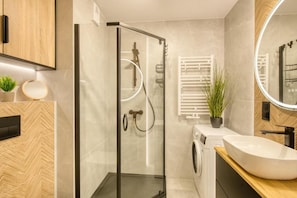 Een moderne badkamer met een douchecabine van glas, een ingebouwde wasmachine en een grote spiegel.